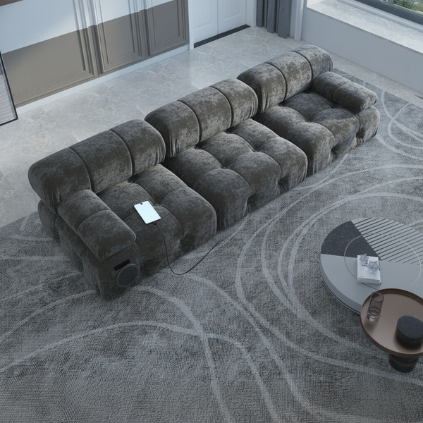 A close-up of a charcoal gray velvet modular sofa showing a discreetly integrated USB charging port and a hidden Bluetooth sp